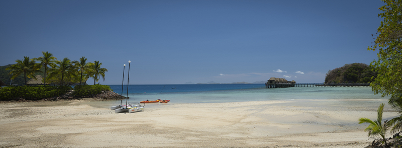 View of Likuliku Lagoon Resort with overwater bungalows sandy beach catamarans and palm trees in Yaro Nadroga Navosa Fiji.