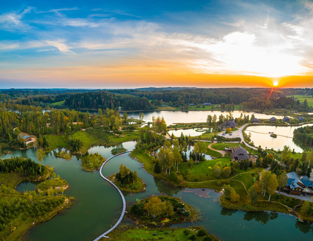 Aerial view of a winding wooden walkway crossing a serene lake surrounded by lush green forests and rolling hills under a vibrant sunset sky in Latvia. Aerial view of a winding wooden walkway crossing a serene lake surrounded by lush green forests and rolling hills under a vibrant sunset sky in Latvia.