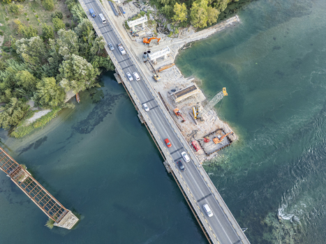 Aerial view of Ura e Bahcallekut bridge construction site with heavy machinery cranes and excavators working near the river and traffic on the road in Bahcallek Shkoder County Albania.