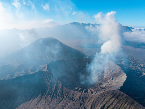 Aerial view of Mount Bromo crater with volcanic smoke rising against a clear blue sky in the Tengger Caldera Tosari East Java Indonesia.