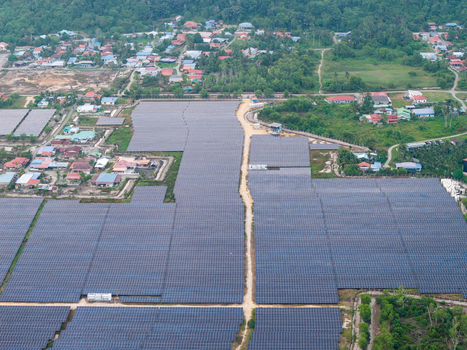 Aerial view of a large scale solar photovoltaic power plant with rows of panels a dirt access road and surrounding residential houses in Central Seberang Perai Penang Malaysia. Aerial view of a large scale solar photovoltaic power plant with rows of panels a dirt access road and surrounding residential houses in Central Seberang Perai Penang Malaysia.
