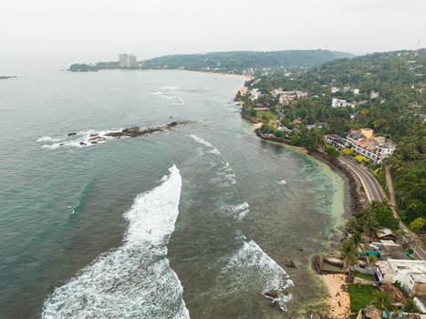 Aerial view of the tropical coastline with turquoise waters breaking waves and lush green vegetation along the shore in Unawatuna Southern Province Sri Lanka.