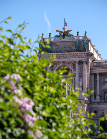 View of the Hofburg Palace featuring its ornate facade statues and golden eagle seen through blooming lilac bushes under a clear blue sky in Vienna Vienna Austria. View of the Hofburg Palace featuring its ornate facade statues and golden eagle seen through blooming lilac bushes under a clear blue sky in Vienna Vienna Austria.
