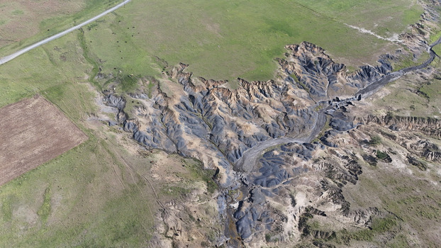 Aerial view of severe soil erosion and deep dongas cutting through green pastures with a dirt road and grazing cattle Pietermaritzburg KwaZulu Natal South Africa.