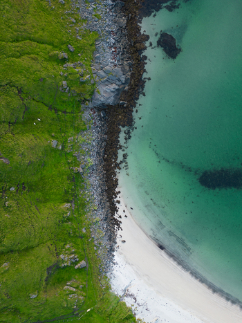Aerial view of the rugged coastline at Tangstad featuring lush green hills a rocky shore and a white sandy beach meeting turquoise waters in Leknes Nordland Norway. Aerial view of the rugged coastline at Tangstad featuring lush green hills a rocky shore and a white sandy beach meeting turquoise waters in Leknes Nordland Norway.
