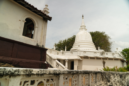 View of a traditional white Buddhist stupa and temple buildings with intricate stone carvings under an overcast sky in Dodanduwa Southern Province Sri Lanka. View of a traditional white Buddhist stupa and temple buildings with intricate stone carvings under an overcast sky in Dodanduwa Southern Province Sri Lanka.