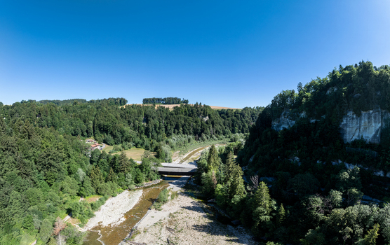 Aerial view of the Sodbachbrucke Sense bridge spanning the river through a lush forested valley with rocky cliffs under a clear blue sky in Heitenried Freiburg Switzerland. Aerial view of the Sodbachbrucke Sense bridge spanning the river through a lush forested valley with rocky cliffs under a clear blue sky in Heitenried Freiburg Switzerland.