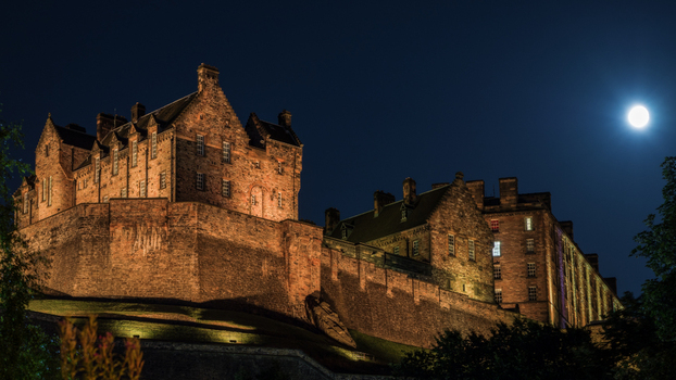 View of the illuminated Edinburgh Castle under a bright full moon in the dark night sky in Edinburgh Scotland United Kingdom. View of the illuminated Edinburgh Castle under a bright full moon in the dark night sky in Edinburgh Scotland United Kingdom.
