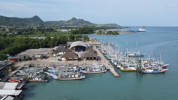 Bakauheni Lampung Indonesia 15 December 2021 Aerial view of Bakauheni harbor with fishing boats moored at the pier traditional buildings with thatched roofs and lush green hills.