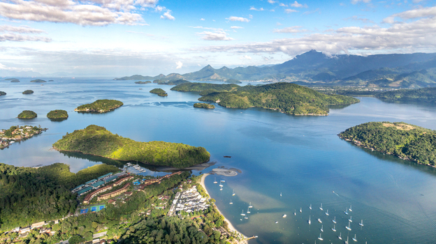 Aerial view of lush islands and coastal waters with sailboats anchored in the bay dense green vegetation and distant mountains in Angra dos Reis Rio de Janeiro Brazil.