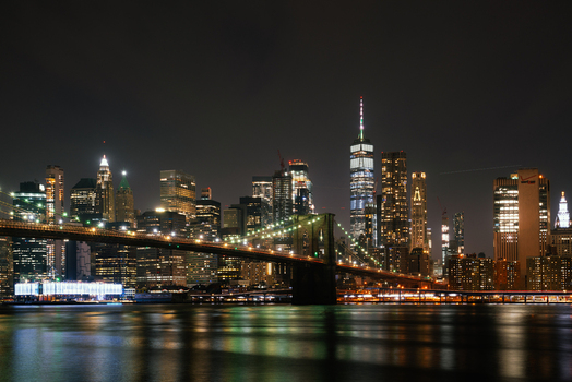 View of the illuminated Brooklyn Bridge and the Manhattan skyline at night with glowing skyscrapers reflecting on the East River in New York New York United States.