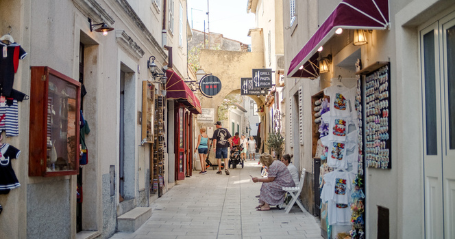 Krk Croatia 19 September 2026 View of a narrow street lined with shops and cafes featuring tourists walking and sitting in the historic town center.