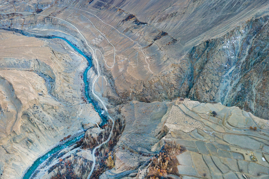 Aerial view of the turquoise river snaking through the arid landscape of Chapursan Valley etched with paths and terraced fields Hunza Nagar Gilgit Pakistan. Aerial view of the turquoise river snaking through the arid landscape of Chapursan Valley etched with paths and terraced fields Hunza Nagar Gilgit Pakistan.