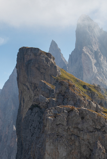 Aerial view of the jagged limestone peaks of the Dolomites with rocky cliffs and patches of green grass under a cloudy sky in Rocca Pietore Veneto Italy.