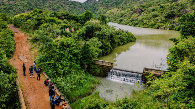 Aerial view of Lamingo Dam with a group of people standing on a dirt path beside the flowing water surrounded by lush green hills and vegetation in Jos Jarawa Plateau Nigeria. Aerial view of Lamingo Dam with a group of people standing on a dirt path beside the flowing water surrounded by lush green hills and vegetation in Jos Jarawa Plateau Nigeria.