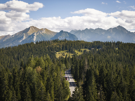 Aerial view of the Tatra Mountains with a winding road cutting through dense pine forests under a blue sky with scattered clouds Poland. Aerial view of the Tatra Mountains with a winding road cutting through dense pine forests under a blue sky with scattered clouds Poland.