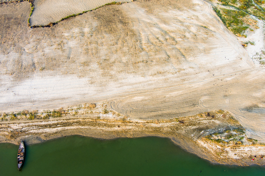Aerial view of a small wooden boat moored along the sandy riverbank with visible tire tracks and sparse vegetation in Rajshahi Rajshahi Division Bangladesh.