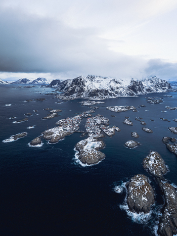 Aerial view of rugged islands scattered across the indigo sea dusted with snow under a brooding sky Henningsv&aelig;r Nordland Norway.