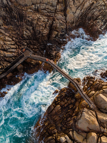 Aerial view of the wooden footbridge at Canal Rocks Bridge spanning over turbulent turquoise ocean waves crashing against the rugged rocky coastline in Yallingup Western Australia Australia. Aerial view of the wooden footbridge at Canal Rocks Bridge spanning over turbulent turquoise ocean waves crashing against the rugged rocky coastline in Yallingup Western Australia Australia.