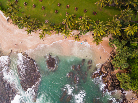 Aerial view of Gintota beach with palm trees a green lawn with sunbeds and turquoise ocean waves crashing on rocks in Galle Southern Province Sri Lanka. Aerial view of Gintota beach with palm trees a green lawn with sunbeds and turquoise ocean waves crashing on rocks in Galle Southern Province Sri Lanka.