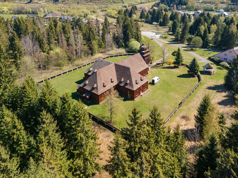Aerial view of the Wooden Articular Church of Svaty Kriz surrounded by a wooden fence and dense pine forest under a clear sky in Svaty Kriz Zilinsky kraj Slovakia.