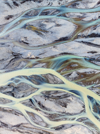 Aerial view of a braided glacial river with turquoise water and dark sediment patterns flowing through gravel bars in Iceland. Aerial view of a braided glacial river with turquoise water and dark sediment patterns flowing through gravel bars in Iceland.