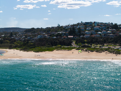Aerial view of a kite surfer on the sandy shore of Northern Beaches with coastal houses on the hillside under a clear blue sky in Northern Beaches Council New South Wales Australia.