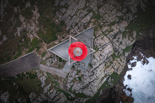 Aerial view of Faro de Punta Nariga lighthouse featuring its red lantern and triangular base on the rocky cliffs of the Atlantic coast in Malpica A Coruna Spain. Aerial view of Faro de Punta Nariga lighthouse featuring its red lantern and triangular base on the rocky cliffs of the Atlantic coast in Malpica A Coruna Spain.