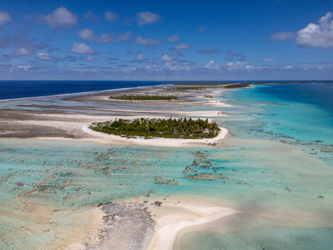 Aerial view of Tikehau atoll featuring turquoise lagoon waters coral reefs and small palm covered islets under a clear blue sky in Tuamotu Archipelago French Polynesia. Aerial view of Tikehau atoll featuring turquoise lagoon waters coral reefs and small palm covered islets under a clear blue sky in Tuamotu Archipelago French Polynesia.
