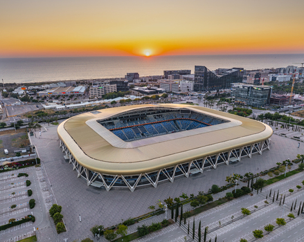 Aerial view of Sammy Ofer Stadium with its distinctive golden roof and blue seating set against the backdrop of a sunset over the Mediterranean Sea in Haifa Haifa District Israel. Aerial view of Sammy Ofer Stadium with its distinctive golden roof and blue seating set against the backdrop of a sunset over the Mediterranean Sea in Haifa Haifa District Israel.