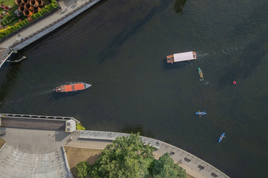 Aerial view of boats gliding on the dark waters of the Brda River reflecting the sky as kayakers paddle along the embankment Bydgoszcz Województwo kujawsko pomorskie Poland. Aerial view of boats gliding on the dark waters of the Brda River reflecting the sky as kayakers paddle along the embankment Bydgoszcz Województwo kujawsko pomorskie Poland.