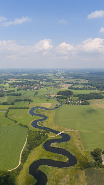 Aerial view of the winding Berkel river flowing through lush green meadows and agricultural fields under a bright blue sky in Almen Gelderland Netherlands. Aerial view of the winding Berkel river flowing through lush green meadows and agricultural fields under a bright blue sky in Almen Gelderland Netherlands.