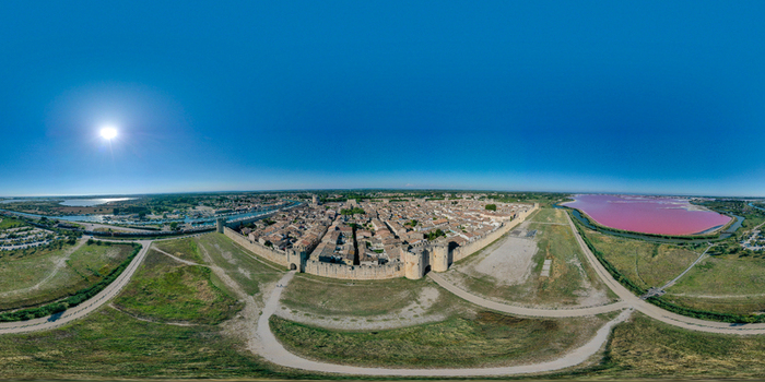 Aerial view of the medieval walled city of Aigues Mortes with stone fortifications and vibrant pink salt pans under a clear blue sky Aigues Mortes Occitanie France.