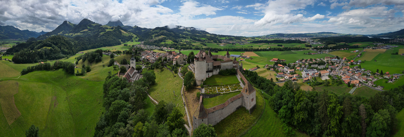 Aerial view of Gruy&egrave;res Castle standing majestically against a backdrop of rolling green hills and dramatic cloud draped mountains Gruy&egrave;res Fribourg Switzerland.