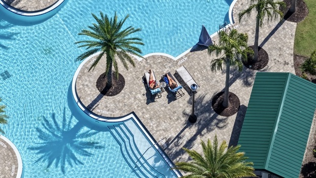 Aerial view of Windward Ranch Boulevard swimming pool with people relaxing on lounge chairs surrounded by palm trees and paved deck in St. Johns County Florida United States. Aerial view of Windward Ranch Boulevard swimming pool with people relaxing on lounge chairs surrounded by palm trees and paved deck in St. Johns County Florida United States.