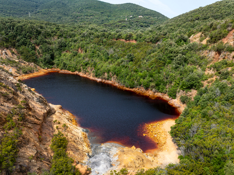 Aerial view of Laghetto delle Conche known as the blood lake with its distinctive deep red water surrounded by lush green hills and rocky terrain in Rio Marina Toscana Italy.