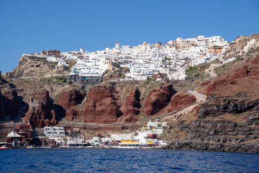 View of white houses and windmills on the volcanic cliffs of Fira overlooking the Aegean Sea under a clear blue sky Fira Greece. View of white houses and windmills on the volcanic cliffs of Fira overlooking the Aegean Sea under a clear blue sky Fira Greece.
