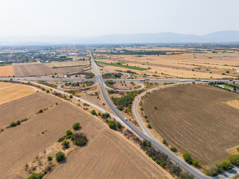 Aerial view of the Trakiya Highway cloverleaf interchange surrounded by vast agricultural fields and dry rural landscape in Bulgaria. Aerial view of the Trakiya Highway cloverleaf interchange surrounded by vast agricultural fields and dry rural landscape in Bulgaria.