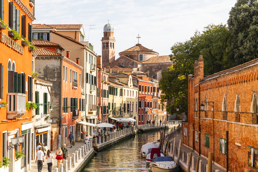 View of a canal lined with historic buildings moored boats and pedestrians walking along the stone embankment in Venice Veneto Italy. View of a canal lined with historic buildings moored boats and pedestrians walking along the stone embankment in Venice Veneto Italy.