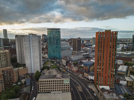 Aerial view of the Birmingham city skyline featuring the iconic Rotunda building modern high rise towers and urban streets under a dramatic cloudy sky in Birmingham England United Kingdom.