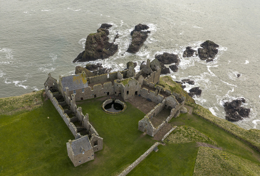 Aerial view of Dunnottar Castle ruins featuring stone walls and a courtyard on a cliff edge overlooking the sea in Stonehaven Scotland United Kingdom. Aerial view of Dunnottar Castle ruins featuring stone walls and a courtyard on a cliff edge overlooking the sea in Stonehaven Scotland United Kingdom.