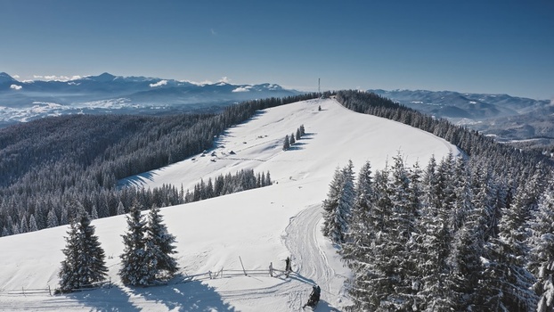 Aerial view of Bukovel ski resort featuring snow covered mountain slopes dense pine forests and clear blue sky in the Carpathian Mountains Bukovel Ivano Frankivsk Oblast Ukraine. Aerial view of Bukovel ski resort featuring snow covered mountain slopes dense pine forests and clear blue sky in the Carpathian Mountains Bukovel Ivano Frankivsk Oblast Ukraine.