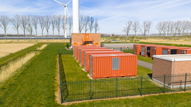 Aerial view of a battery energy storage system with orange containers wind turbines and a brick utility building in Middelharnis Zuid Holland Netherlands.