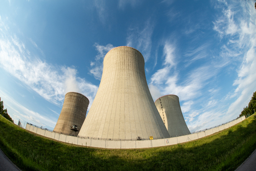 View of the large concrete cooling towers of a nuclear power plant under a bright blue sky with wispy clouds in Czechia. View of the large concrete cooling towers of a nuclear power plant under a bright blue sky with wispy clouds in Czechia.