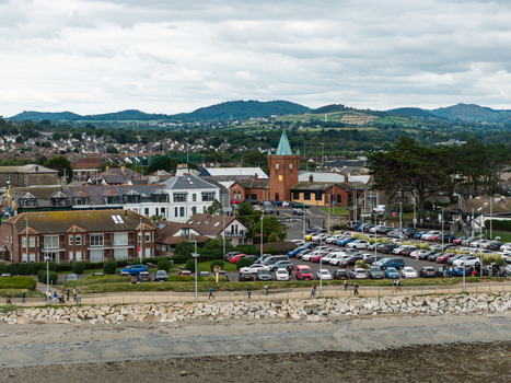 Aerial view of the historic railway station clock tower and coastal town with a parking lot residential buildings and hills in the background in Newcastle Northern Ireland United Kingdom. Aerial view of the historic railway station clock tower and coastal town with a parking lot residential buildings and hills in the background in Newcastle Northern Ireland United Kingdom.