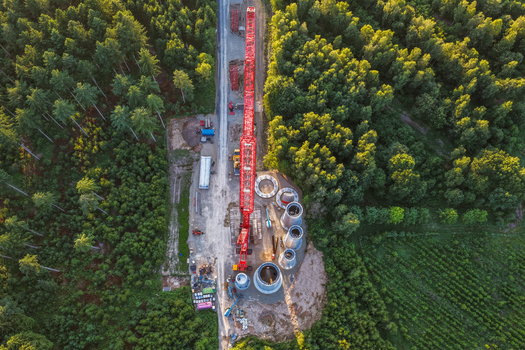 Aerial view of a construction site with a large red crane and wind turbine tower segments nestled within a dense forest in Hofgeismar Hessen Germany. Aerial view of a construction site with a large red crane and wind turbine tower segments nestled within a dense forest in Hofgeismar Hessen Germany.