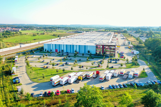 Forchheim Germany 10 March 2026 Aerial view of the Simon Hegele logistics center featuring a large warehouse parking lots with trucks and cars and surrounding green fields.