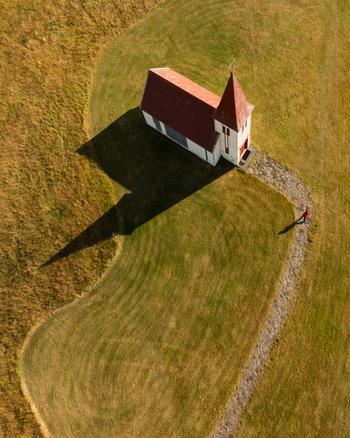 Aerial view of the stark white church with its red roof stands out in the Icelandic landscape casting a long shadow Hellnar Sn&aelig;fellsb&aelig;r Iceland.