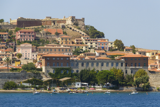 View of the vibrant town cascading down the hillside towards the shimmering sea with historic buildings and terracotta roofs Portoferraio Tuscany Italy. View of the vibrant town cascading down the hillside towards the shimmering sea with historic buildings and terracotta roofs Portoferraio Tuscany Italy.