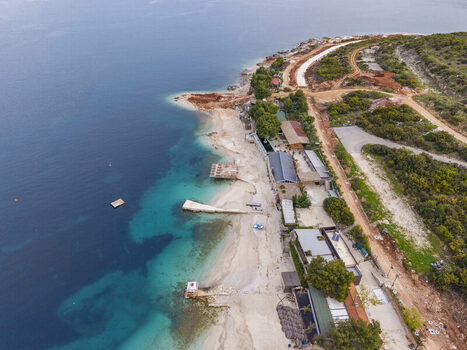 Aerial view of the coastline in Ksamil featuring turquoise waters sandy beach small piers and nearby buildings surrounded by Mediterranean vegetation in Ksamil Vlore County Albania. Aerial view of the coastline in Ksamil featuring turquoise waters sandy beach small piers and nearby buildings surrounded by Mediterranean vegetation in Ksamil Vlore County Albania.